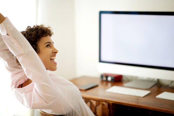 istock happy young woman sitting by computer with arms raised 1185317076