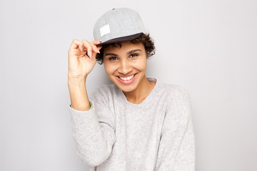 Close up portrait of happy young african american woman smiling with cap by white wall
