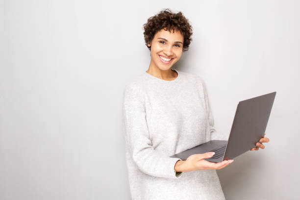 istock smiling young woman holding laptop computer by white background 1185317091