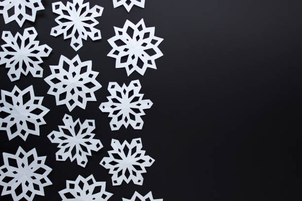 Black and white Christmas winter festive simple background with large white handmade paper snowflakes on black background.