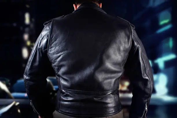Closeup photo of a man in black leather biker jacket standing on night citylights background.