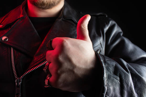 istock Biker in black leather jacket with skull rings showing thumbs up. 1185321500