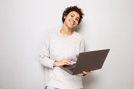 Portrait of beautiful young woman posing by white wall with laptop computer