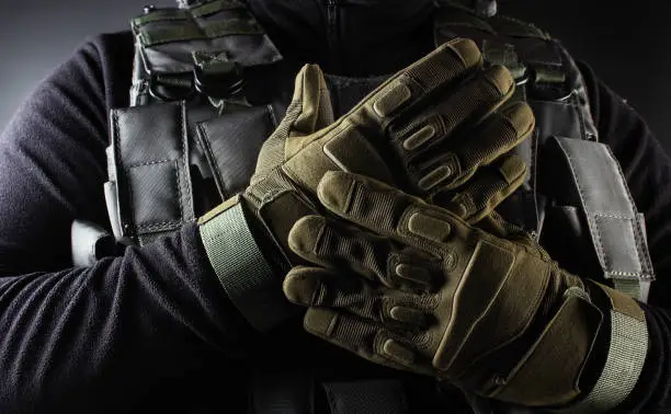 Photo of a fully equipped soldier in black armor tactical vest and gloves standing on black background closeup front view.