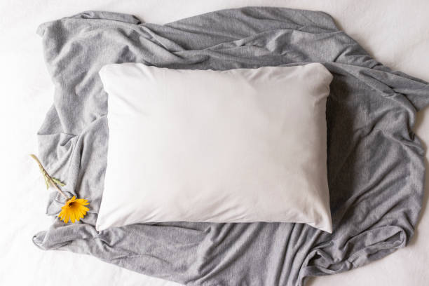 istock Plain white pillowcase on a grey and white textile background with a yellow daisy flower 1185325310