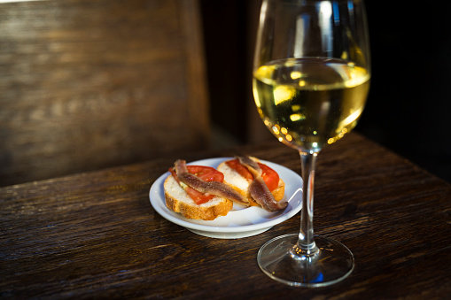 This is a close up image capture of a glass of white wine and sardine bread tapas at a Spain restaurant bar.