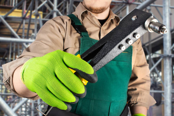 istock Worker in green overall outfit with protective gloves holding riveter hand tool. 1185325353