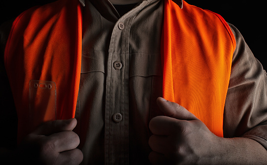 Photo of a worker in orange jacket outfit shaded on black background.