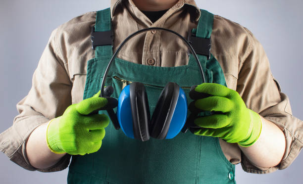 Worker in green overall outfit with protective gloves holding headphones. stock photo