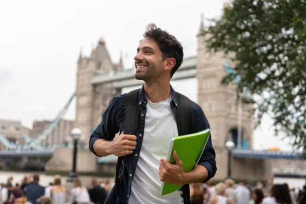 Portrait of a happy student in London holding a notebook and smiling near Tower Bridge - education concepts