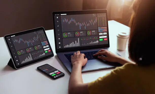 Photo of Stock exchange market concept, businesswoman trader looking on laptop and tablet, smartphone with graphs analysis candle line in office room, diagrams on screen.