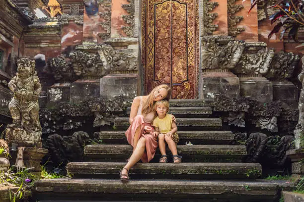 Photo of Mom and son travelers in the background of Pura Taman Kemuda Saraswati Temple in Ubud, Bali island, Indonesia BANNER, long format Traveling with children concept