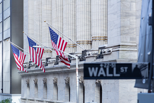 blured wall street sign with new york stock exchange in focus flags as background