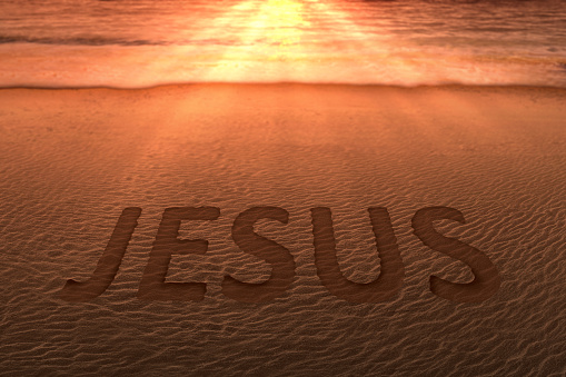 Jesus text on the sandy beach with a sunset sky background