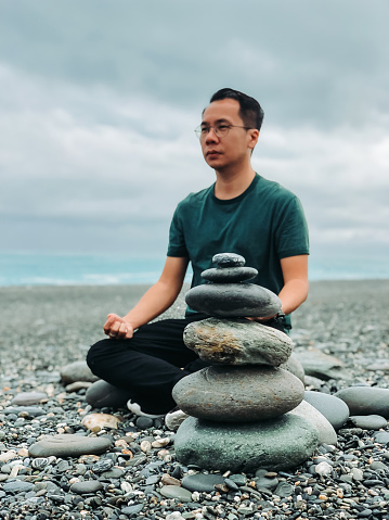 an asian chinese male tourist from malaysia meditation at the beach in taiwan with rock stacked up