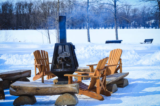 Wooden benches and chairs with fireplace charged with firewood, in the resting place during winter season. Wood-burning fire pit with removable fire pan and with wide bar ribs and handles. Outdoor chimney. stock photo