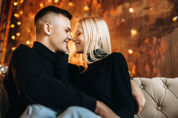istock Side view portrait of a beautiful young couple sitting on sofa embracing . Man and woman kissing and smiling at home. 1185347324