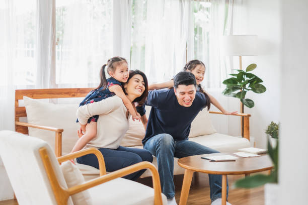 glückliche asiatische familie, die zusammen auf dem sofa spielt, wohnzimmer zu hause - joy of living stock-fotos und bilder