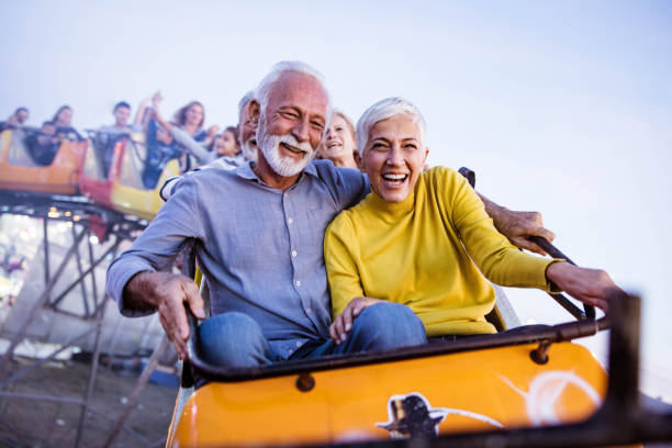 Carefree seniors having fun on rollercoaster at amusement park. Cheerful senior couple having fun while riding on rollercoaster at amusement park. Copy space. rollercoaster photos stock pictures, royalty-free photos & images