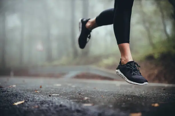 Unrecognizable athletic woman running on the road during foggy day in nature. Copy space.