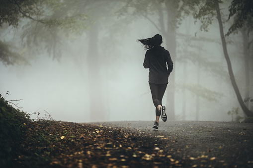 Rear view of female athlete jogging in foggy forest. Copy space.