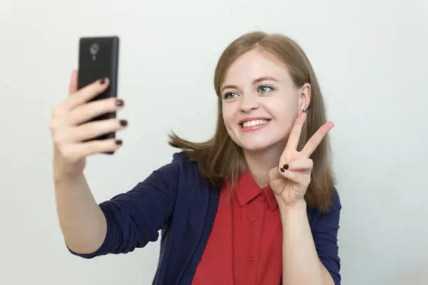 Photo of Smiling young caucasian girl woman taking selfie or making a video call on mobile phone