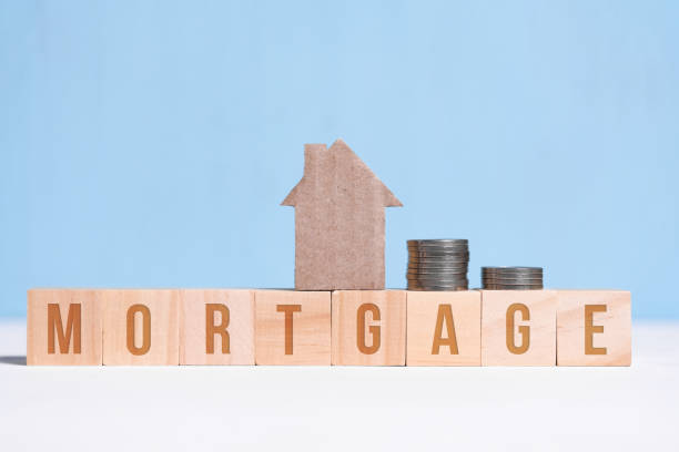 Cardboard cutout house and coins on cubes with inscription mortgage on blue background. Cardboard cutout house and coins on cubes with inscription mortgage on blue background. Concept of hypothec, debt, credit. hypothecary stock pictures, royalty-free photos & images