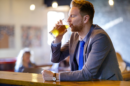 Young businessman having a glass of draft beer, leaning on the bar counter