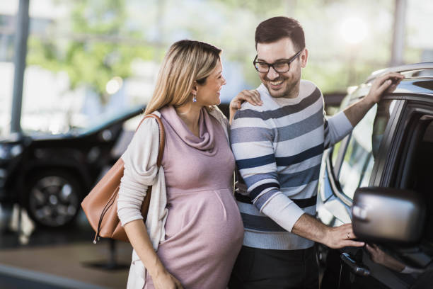 feliz pareja embarazada hablando mientras compra un coche nuevo en una sala de exposición. - common family new togetherness fotografías e imágenes de stock