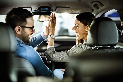 Young happy couple sitting inside of their new car and giving each other high-five.