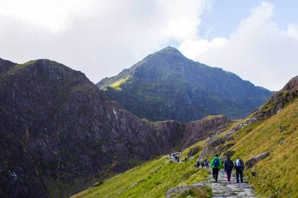 People walking to the summit of a mountain through a pathway surrounded by beautiful landscapes in Snowdonia, Wales People walking to the summit of a mountain through a pathway surrounded by beautiful landscapes in Snowdonia, Wales snowdonia national park stock pictures, royalty-free photos & images