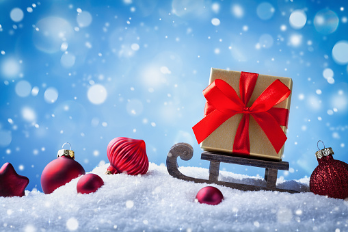 Christmas or New Year greeting card. Golden gift or present box on sledge in snowy background.