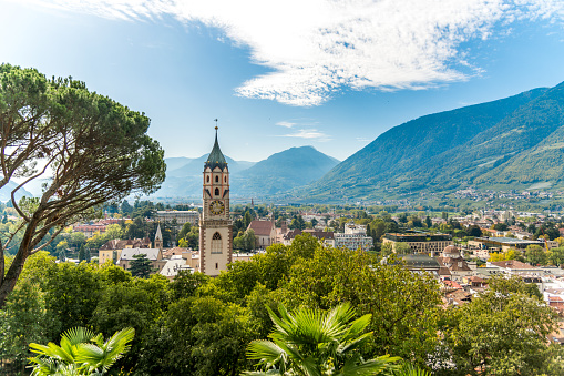 View of Meran old town in South Tyrol with mountains, blue sky and parish church of St. Nicholas