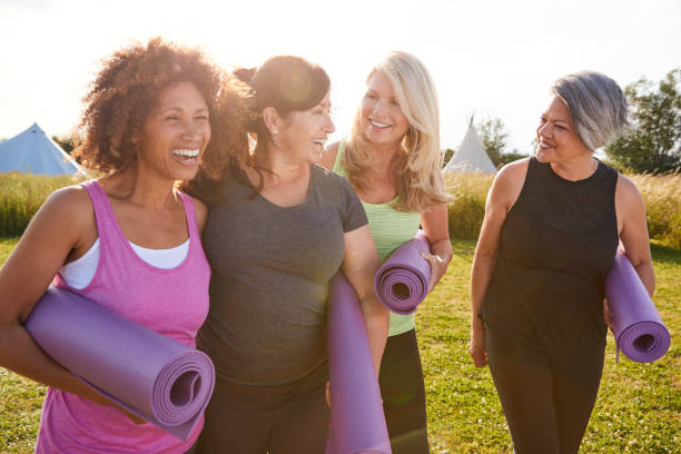 group of mature female friends on outdoor yoga retreat walking along path through campsite - senior adult sport yoga exercising imagens e fotografias de stock
