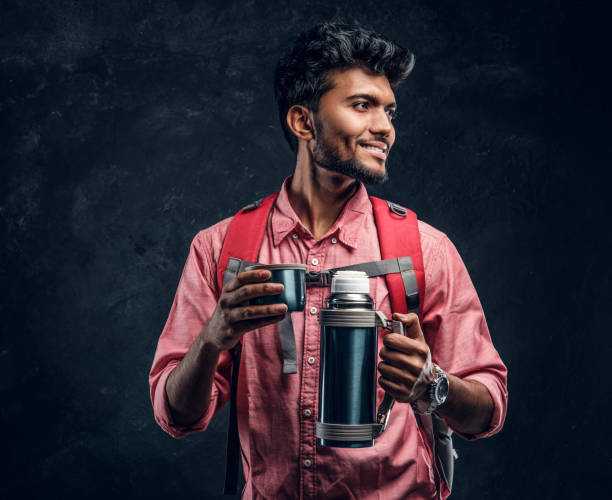 istock Young stylish hiker with backpack holding a cup with tea while smiling and looking sideways. 1185393525