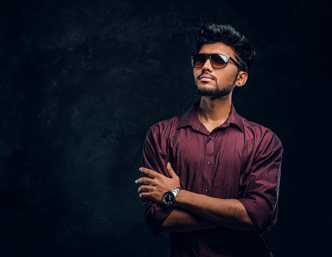 Vogue, moda, estilo. Guapo joven indio con una camisa elegante y gafas de sol posando con los brazos cruzados. photo