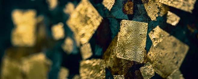 Abstract textured background of gold leaf square shapes on a grungy old rusty weathered metal background.