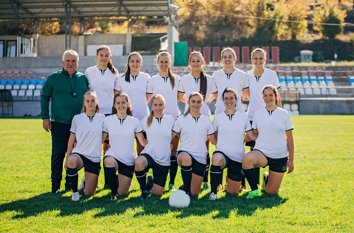 Group of women and man coach, team photo on soccer field.