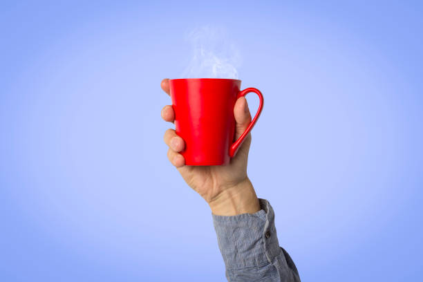 istock Male hand holding a red cup with hot coffee or tea on a light blue background. Breakfast concept with hot coffee or tea 1185406192