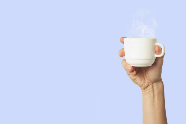 istock Male hand holding a white cup with hot coffee or tea on a light blue background. Breakfast concept with hot coffee or tea 1185406889
