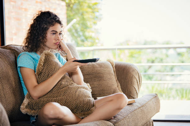 istock Hispanic curly hair young woman selecting channels with remote control watching tv on a sofa 1185407042