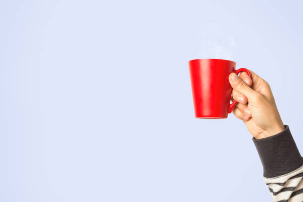 istock Male hand holding a red cup with hot coffee or tea on a light blue background. Breakfast concept with hot coffee or tea 1185407608