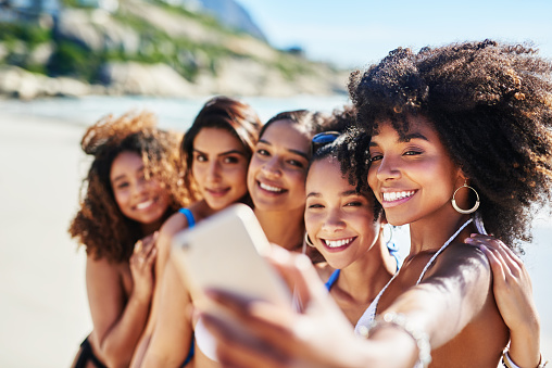 Shot of a group of happy young women taking selfies together at the beach