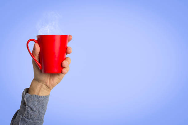 istock Male hand holding a red cup with hot coffee or tea on a light blue background. Breakfast concept with hot coffee or tea 1185410344