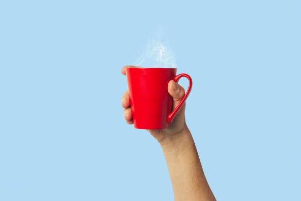 istock Male hand holding a red cup with hot coffee or tea on a light blue background. Breakfast concept with hot coffee or tea 1185410353