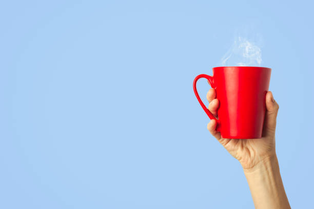 istock Female hand holding a red cup with hot coffee or tea on a light blue background. Breakfast concept with hot coffee or tea 1185410457