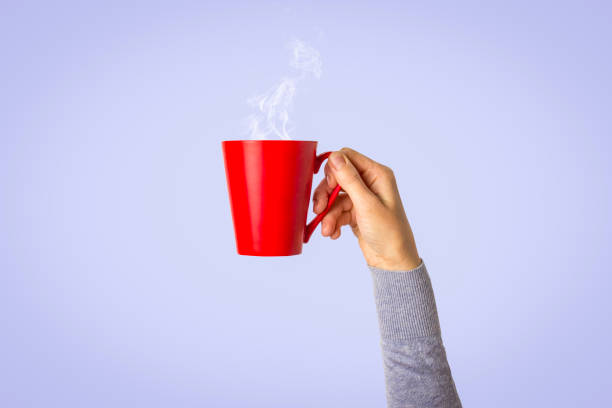 istock Female hand holding a red cup with hot coffee or tea on a light blue background. Breakfast concept with hot coffee or tea 1185410487