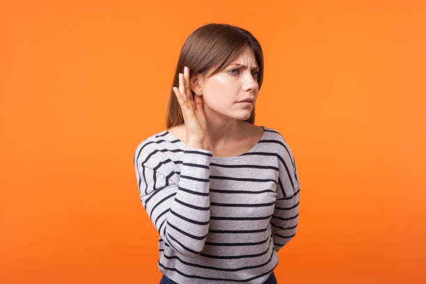 portrait of attentive nosy young woman with brown hair in long sleeve striped shirt. indoor studio shot isolated on orange background - spy secrecy top secret mystery imagens e fotografias de stock