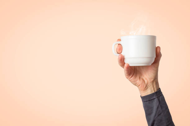 istock Female hand holding a white cup with hot coffee or tea on a light pink background. Breakfast concept with hot coffee or tea 1185411274