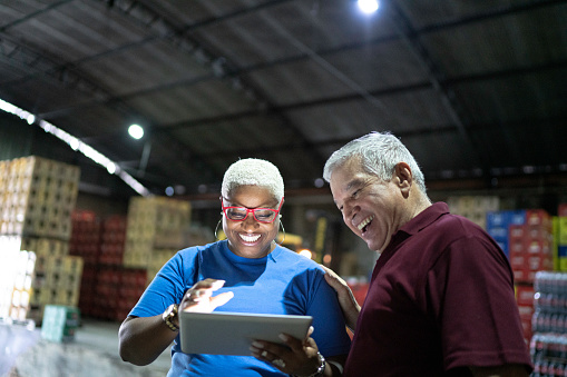 Partners celebrating good news and using digital tablet at warehouse